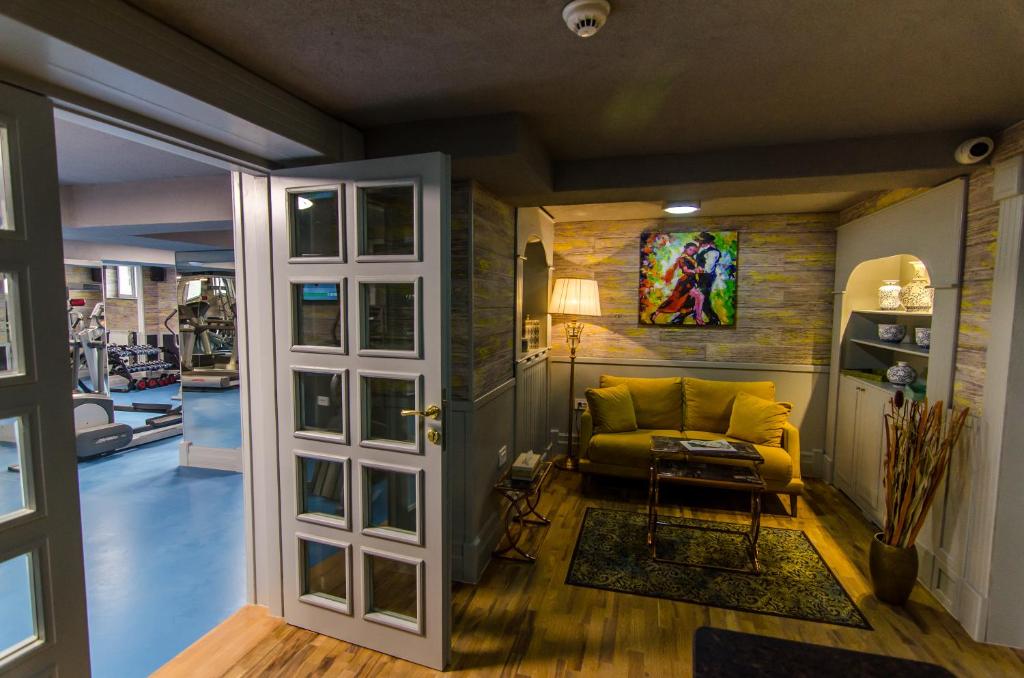 Seating area with yellow sofa, coffee table and decorative lamp, frosted glass doors opening to a blue-walled gym at Hotel Lido by Phoenicia in Bucharest