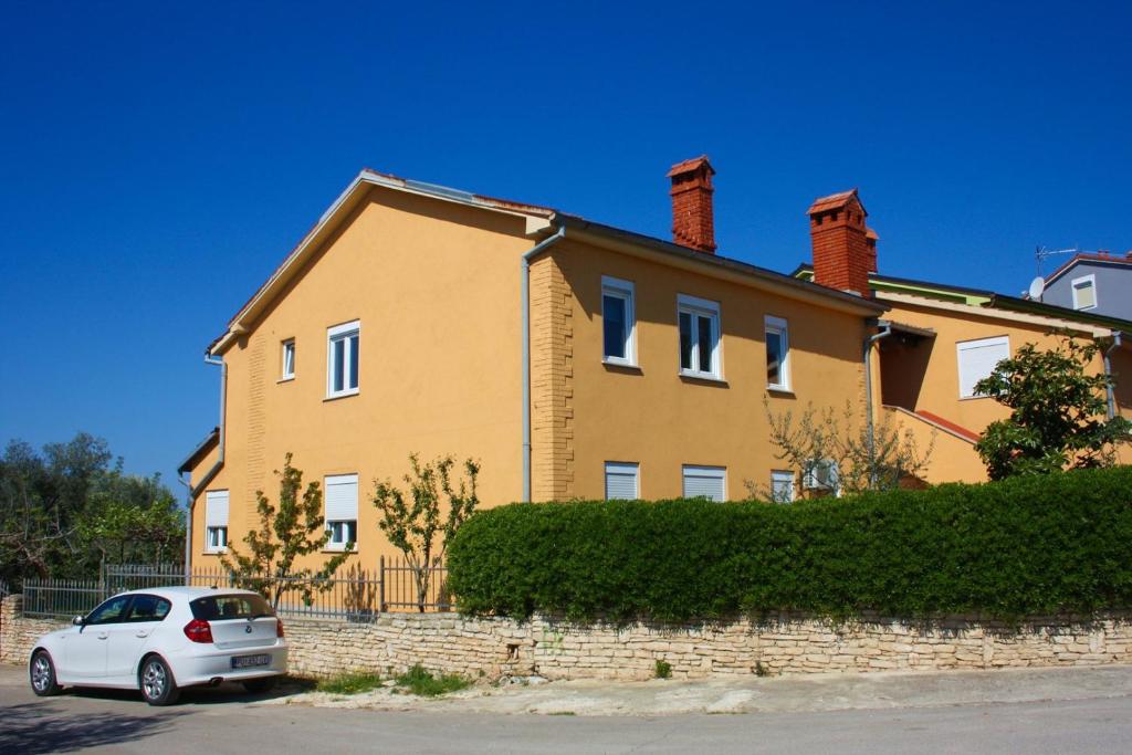 a white car parked in front of a yellow house at Apartments Drandic in Fažana