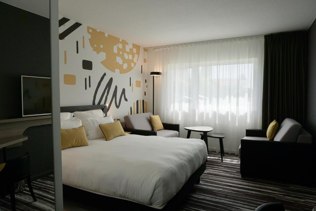 ein Hotelzimmer mit einem großen Bett und einem Sofa in der Unterkunft Golden Tulip Roissy Saint Witz in Saint-Witz