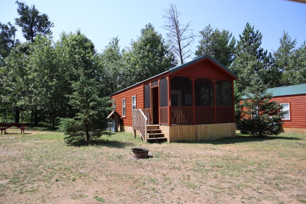 a small red cabin with a porch and a fence at Bonanza Camping Resort in Wisconsin Dells