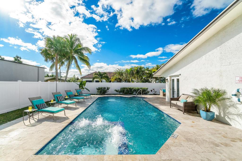 a swimming pool in a backyard with blue chairs and a white wall at Beach Luxury, 4B- 3B Heated Pool, Infinity Spa, Cabana with Outdoor Kitchen and TV, BBQ, Golden Tee Arcade, Walk to Beach! Sleeps 10 in West Palm Beach