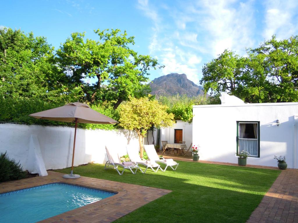 a backyard with a pool and chairs and an umbrella at Avenues Guest House in Stellenbosch
