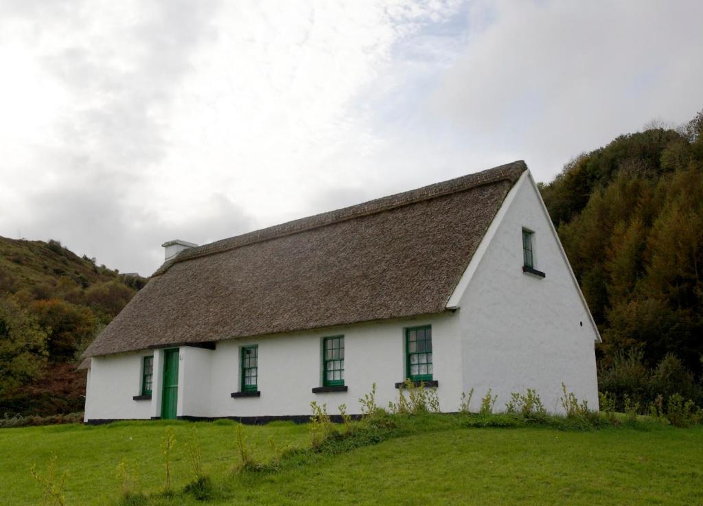 a white house with a brown roof on a green field at Corofin Lake Cottages in Corrofin