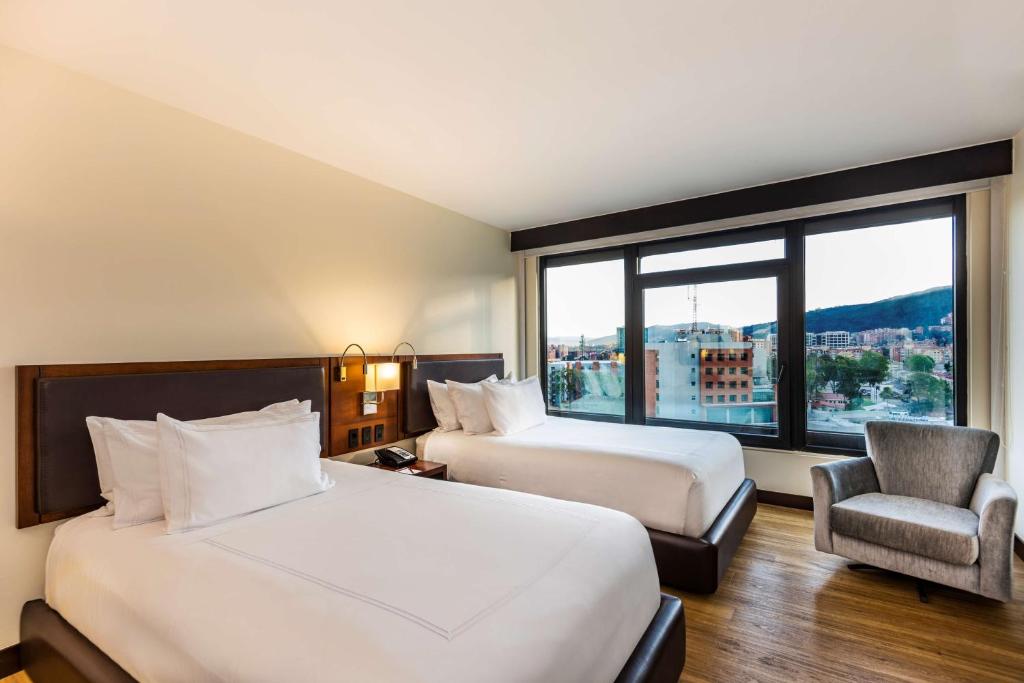 um quarto de hotel com duas camas e uma cadeira e uma janela em NH Collection Bogota WTC Royal em Bogotá