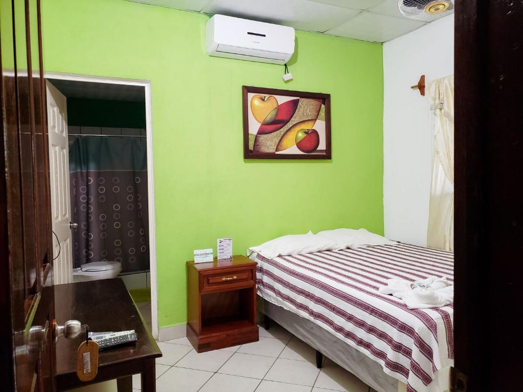 1 dormitorio con paredes verdes, 1 cama y 1 mesa en Hotel y Restaurante Las Gardenias, en El Remate