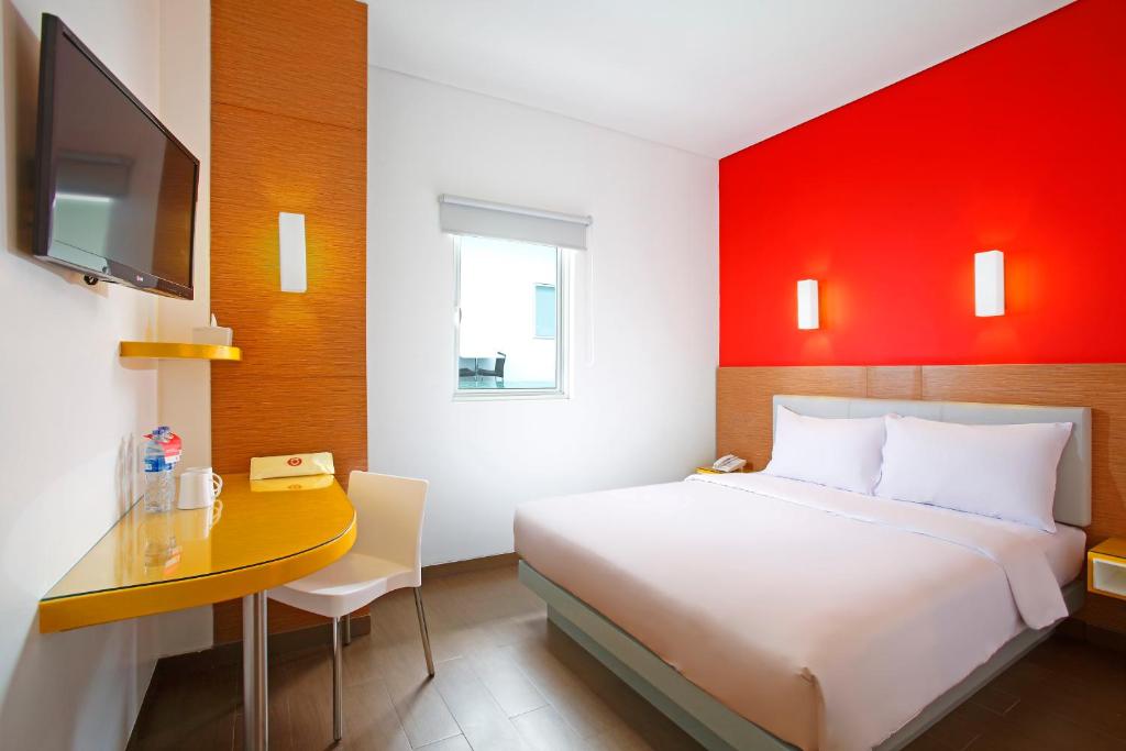 a bedroom with a bed and a desk with a television at Amaris Hotel Sunset Road - Bali in Kuta
