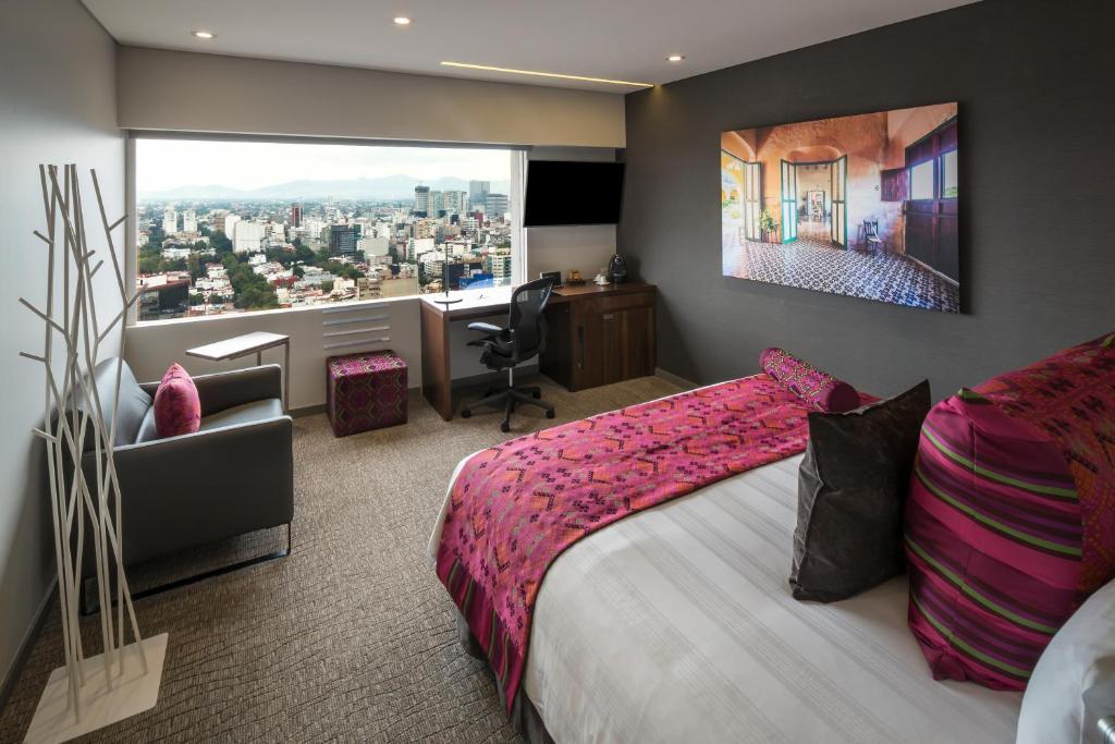 A bright guest room places a bed, work desk, armchair, and city outlook around a large window.