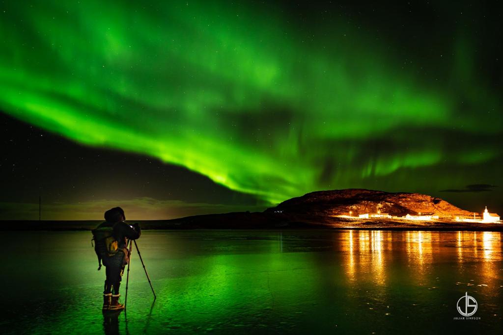 un hombre está de pie en el agua bajo la aurora en Helgafell, en Stykkishólmur