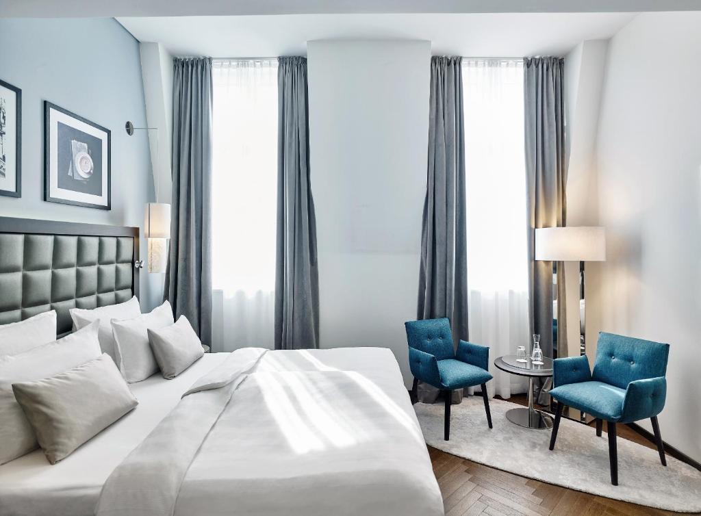a bedroom with a bed and two blue chairs at Steigenberger Hotel Herrenhof in Vienna