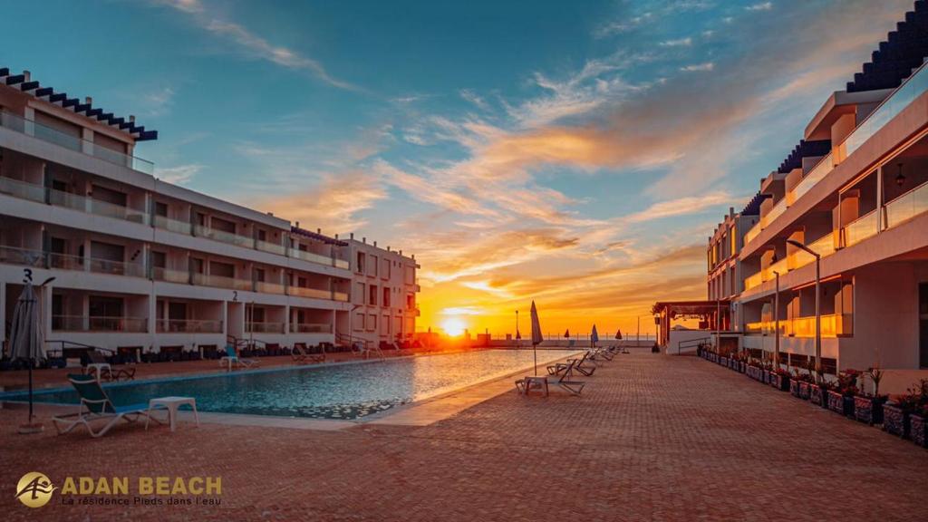 a hotel with a swimming pool in front of a sunset at Adan Beach Residence, Beach Front Apartments in Aourir