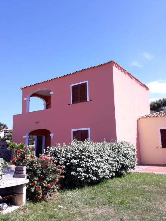 une maison rose avec des fleurs devant elle dans l'établissement casa rosa nel residence mirice con piscina ,wifi,climatizzatore - vicino al mare, à Aglientu