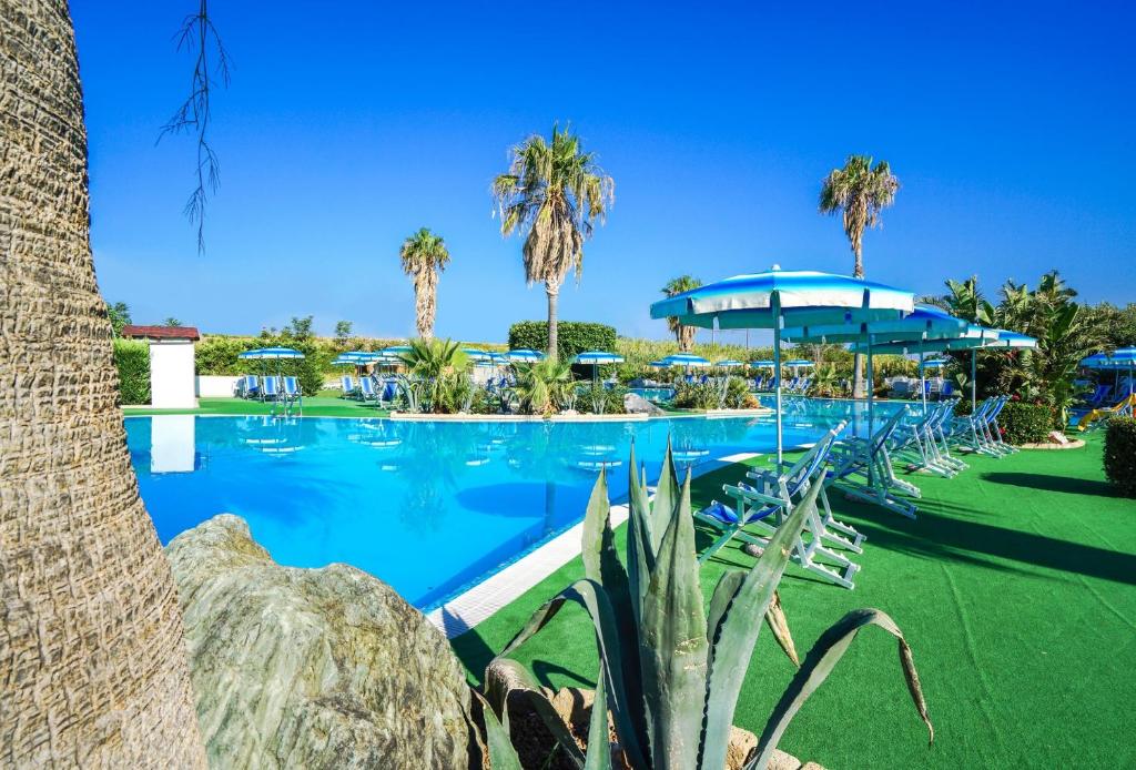 una piscina con palmeras y sombrillas azules en Villaggio Residence Bahja, en Paola