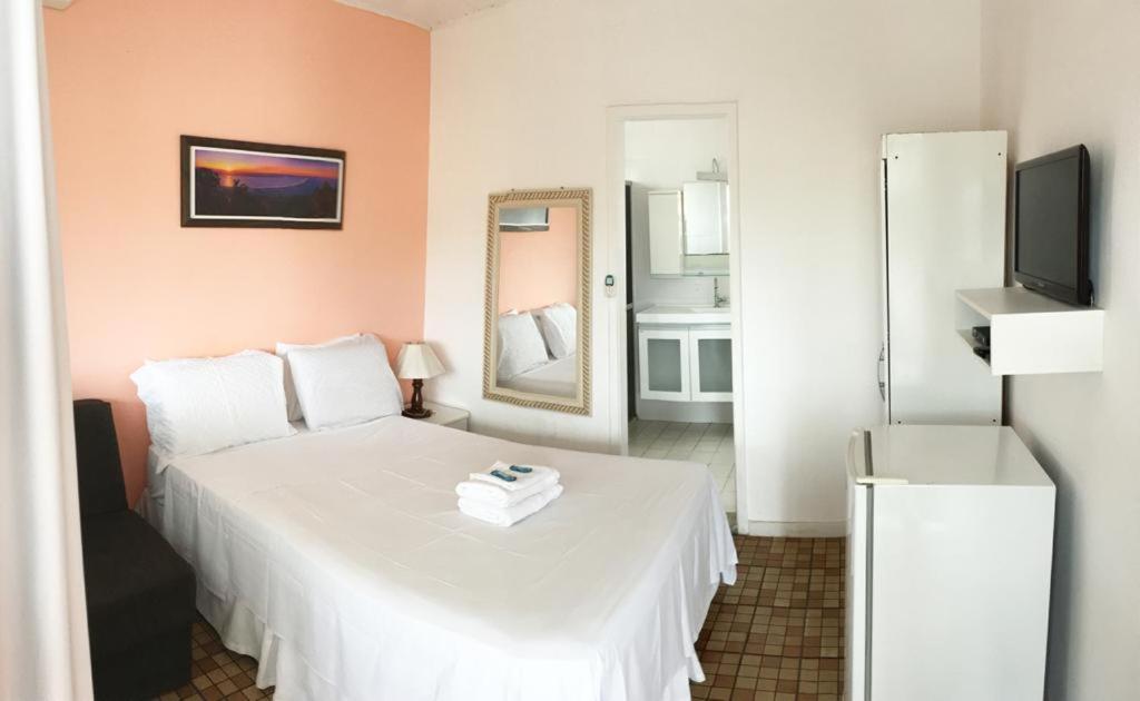 1 dormitorio con 1 cama blanca y TV en Nascimento Suites en Búzios