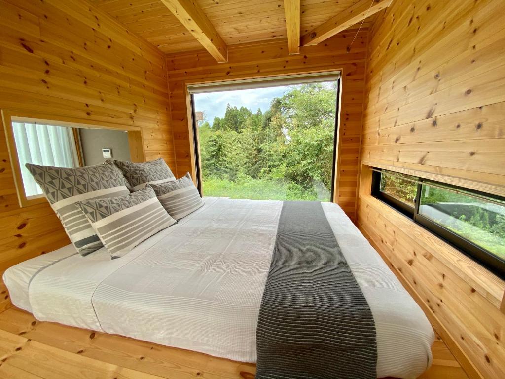 ein Schlafzimmer mit einem großen Fenster in einem Blockhaus in der Unterkunft Le Lodge Mimitsu in Hyuga