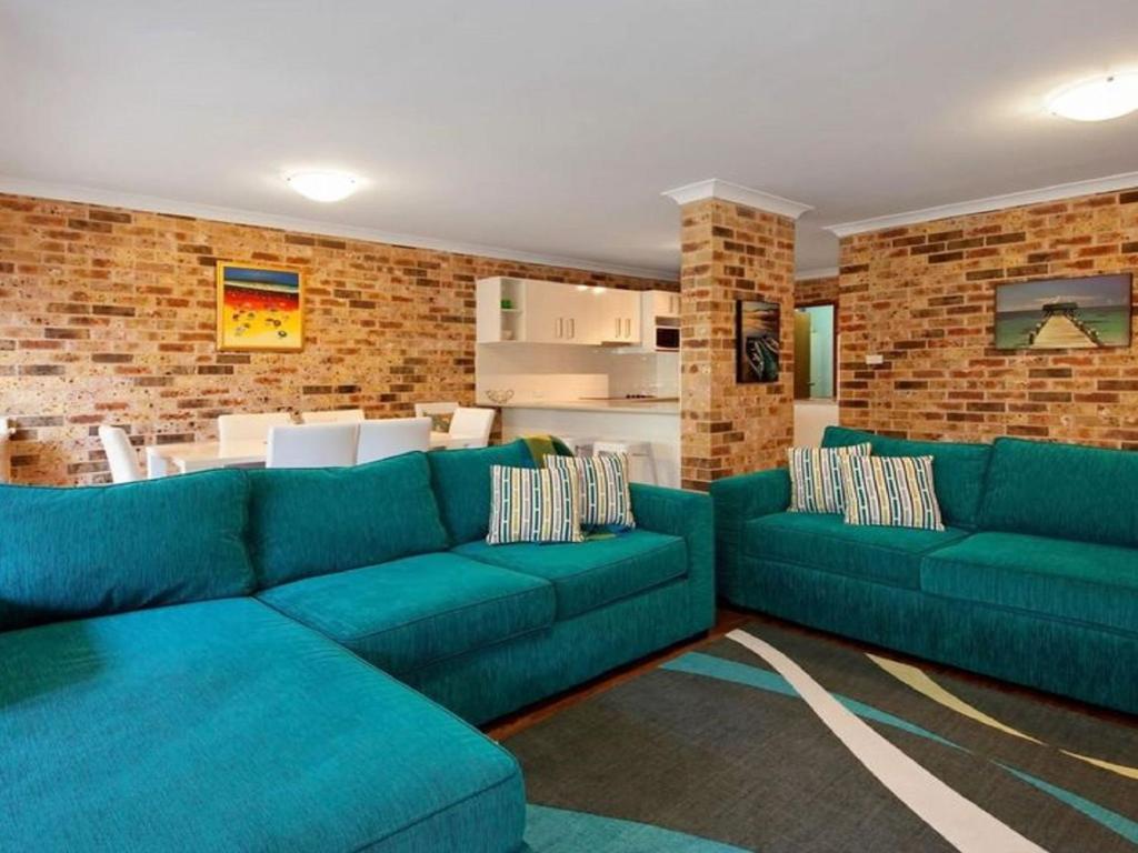 un soggiorno con divani blu e un muro di mattoni di Bay Parklands 69 large unit with views pool tennis court and spa a Nelson Bay