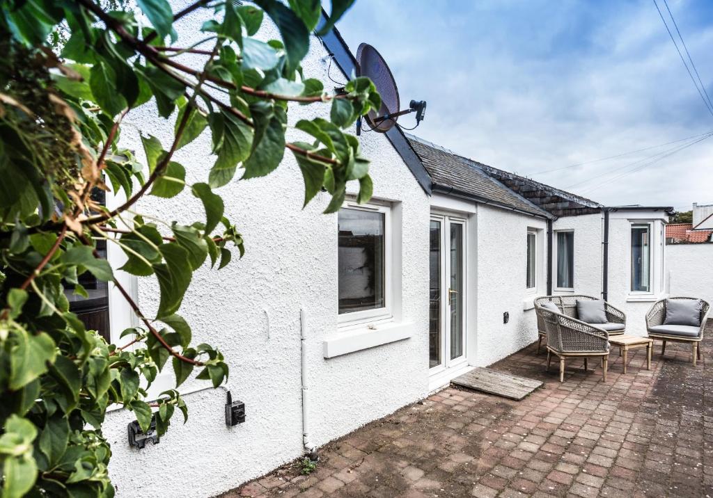 a white house with a patio with chairs and a table at Summerside Cottage in Gullane