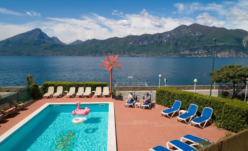 una piscina con un flamenco y sillas y un cuerpo de agua en Hotel Caribe - Garda Lake Collection, en Brenzone sul Garda