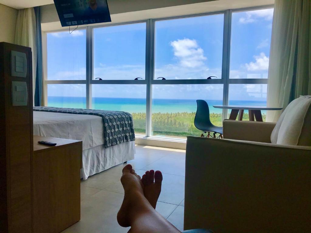 a persons feet in a bedroom with a view of the ocean at Paiva Flat Home Stay - Barra de Jangada in Recife