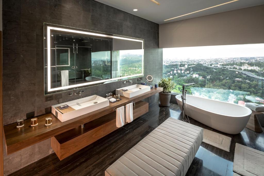 A dramatic bathroom with twin vanities, a freestanding tub, and a broad city view.