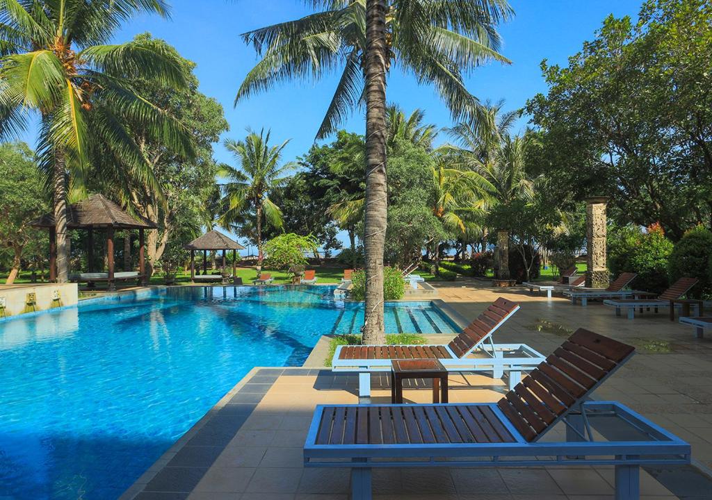 einen Pool mit zwei Stühlen und einem Tisch neben einer Palme in der Unterkunft The Jayakarta Suites Komodo Flores in Labuan Bajo