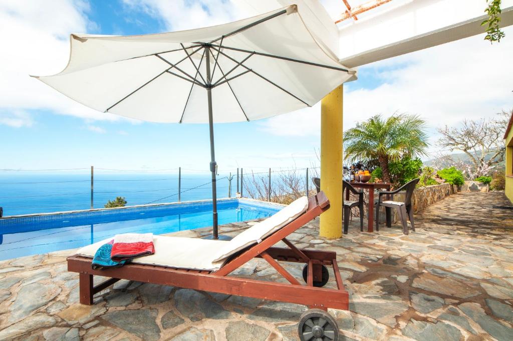 a lounge chair with an umbrella next to a swimming pool at CASA EMILIA in Tijarafe