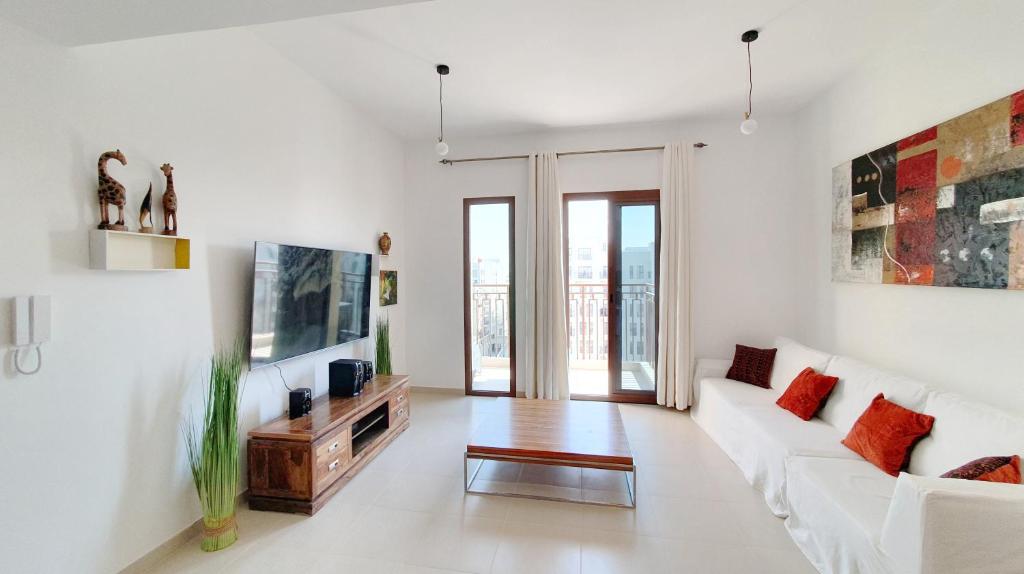 a white living room with a white couch and a tv at Spacious 2 Bedroom Apartment DXB in Dubai