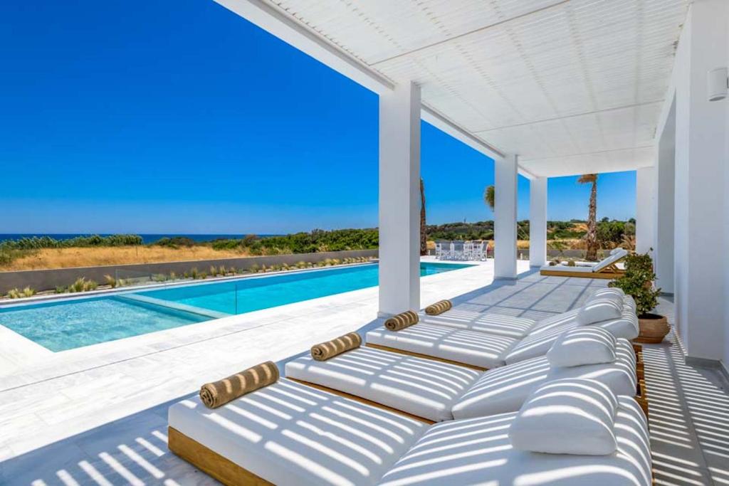 a row of chaise lounge chairs on a patio with a swimming pool at Seashore Beachfront Villa in Lachania