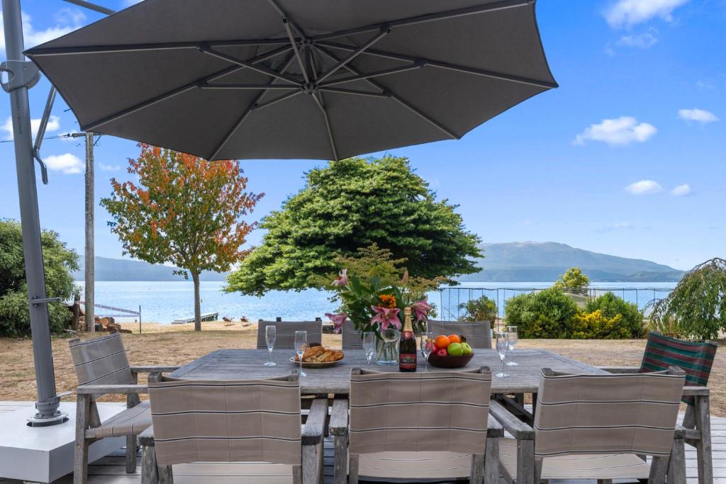 a table with an umbrella and a table with chairs at Winstone Cottage - Waterfront Lake Tarawera Home in Lake Tarawera