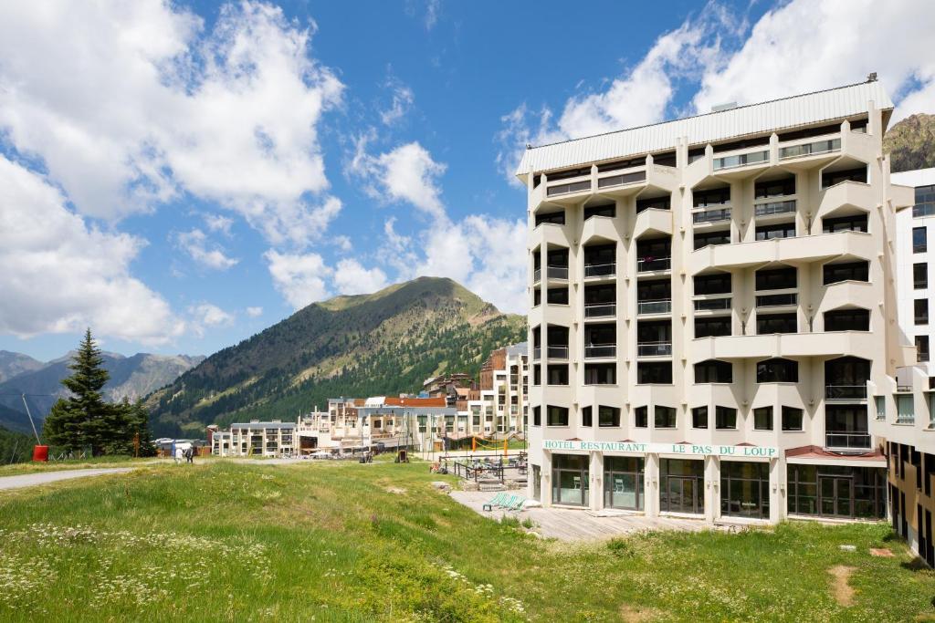 a large white building with mountains in the background at SOWELL HOTELS Le Pas du Loup in Isola 2000