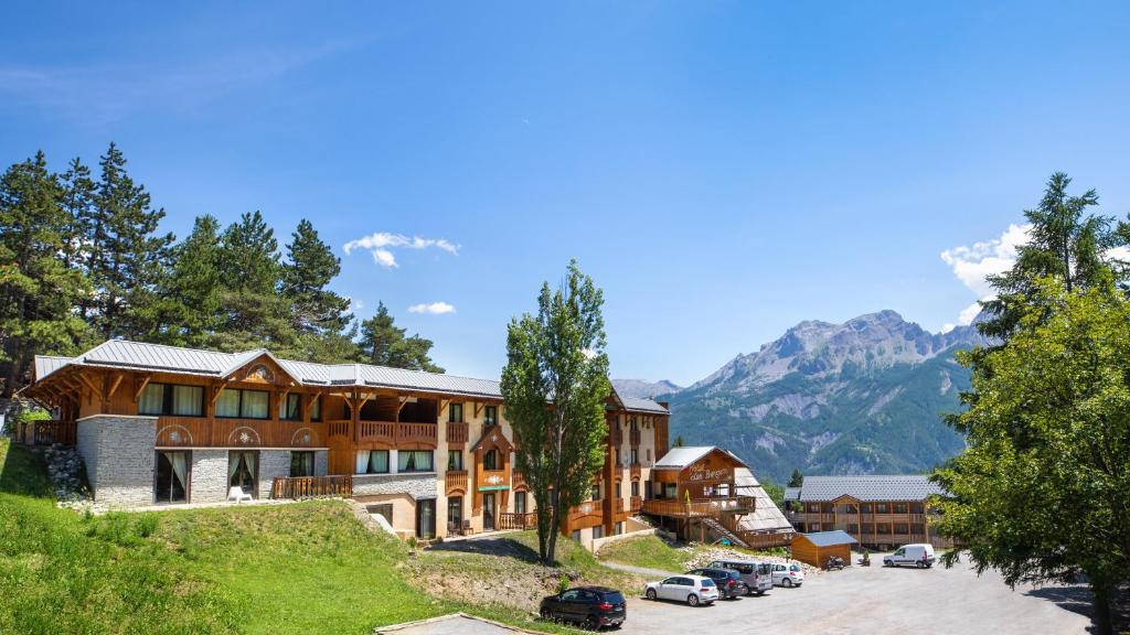 un grand bâtiment en bois avec des voitures garées dans un parking dans l'établissement SOWELL Family Les Bergers, à Pra-Loup