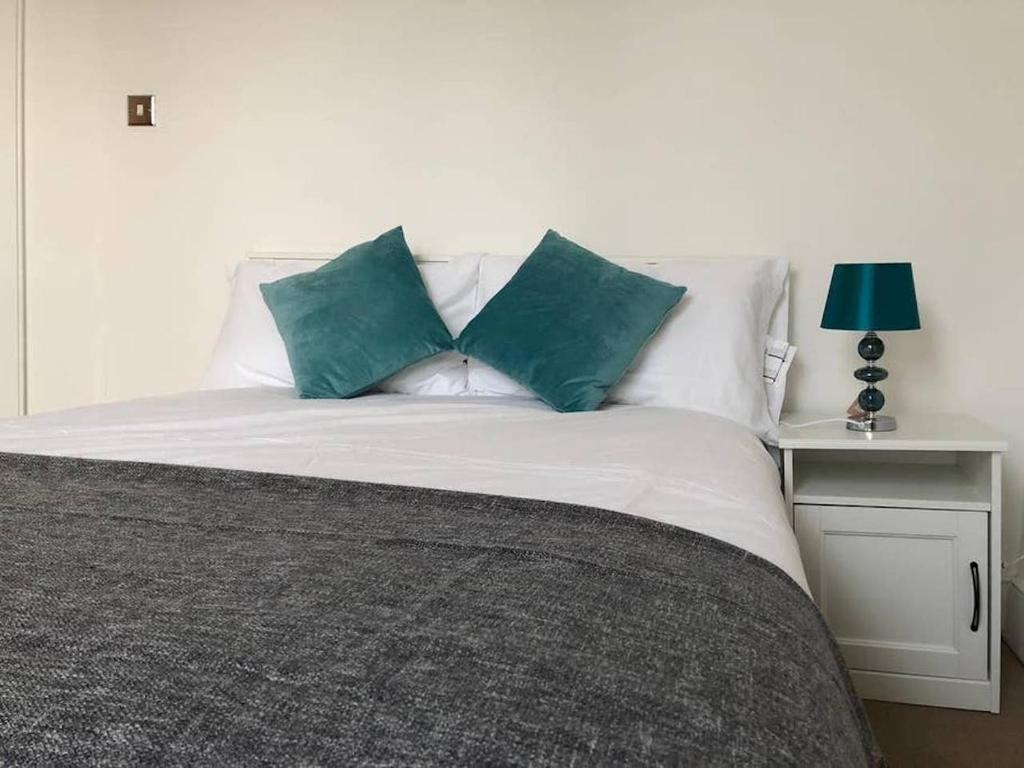 a white bed with two green pillows on it at Eurostar Budget Rooms - Next to Kings Cross & Eurostar Train Station in London