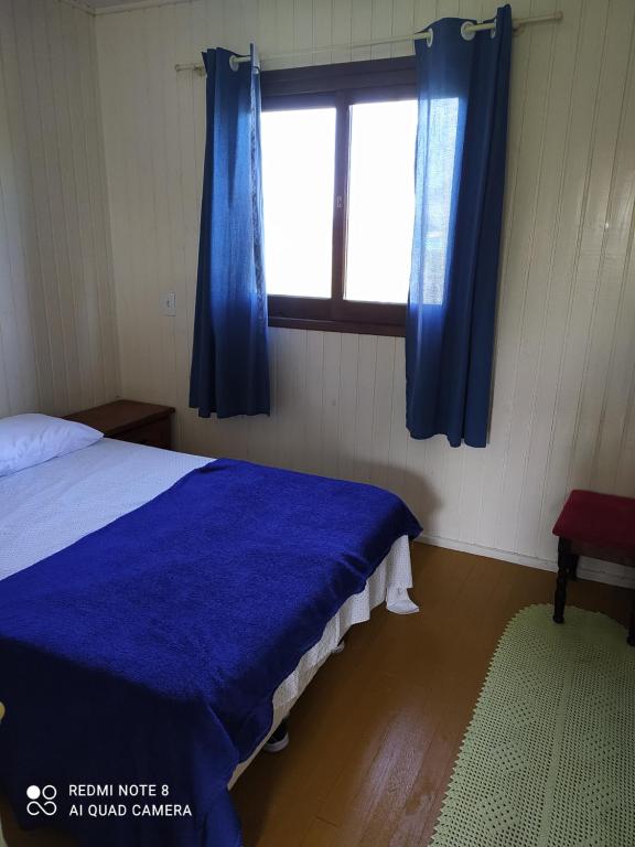 una camera con letto e finestra con tende blu di Casa de Praia. Lugar sossegado para recarregar as energias. a Passo de Torres