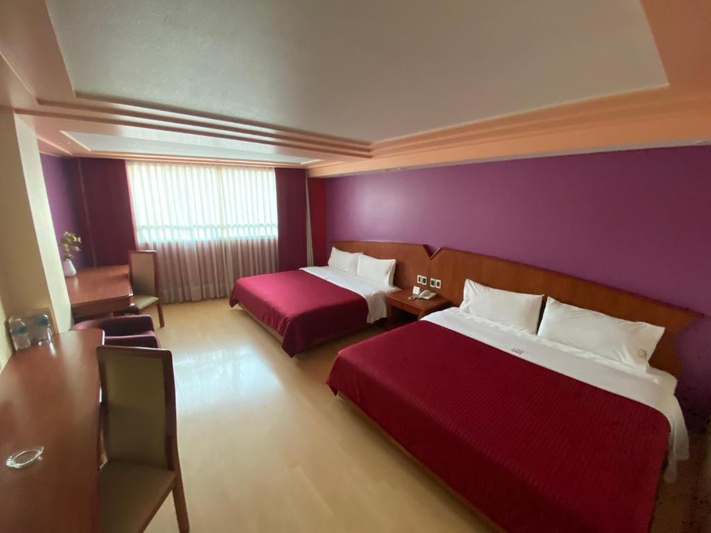 A two-bed room with a long table, purple feature wall, and curtained window.