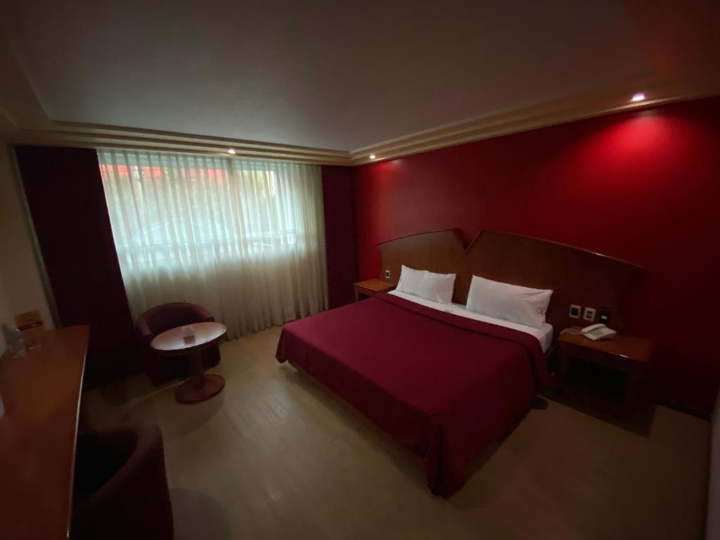 A warmly lit bedroom with a red accent wall, double bed, sitting area, and desk.