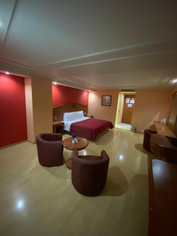 A spacious room with one large bed, lounge chairs, a round table and a work desk.