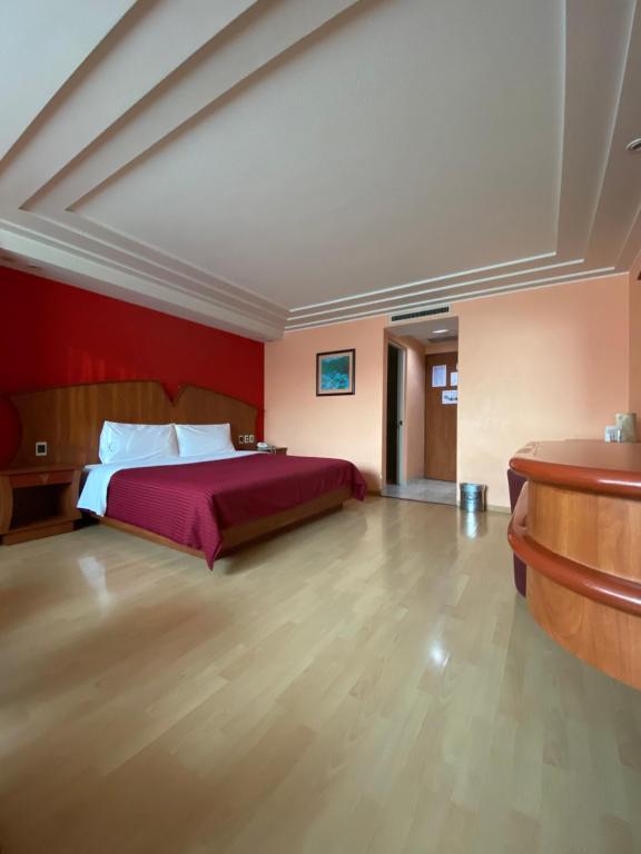 A bright room with one large bed, a red feature wall and a built-in desk or dresser.