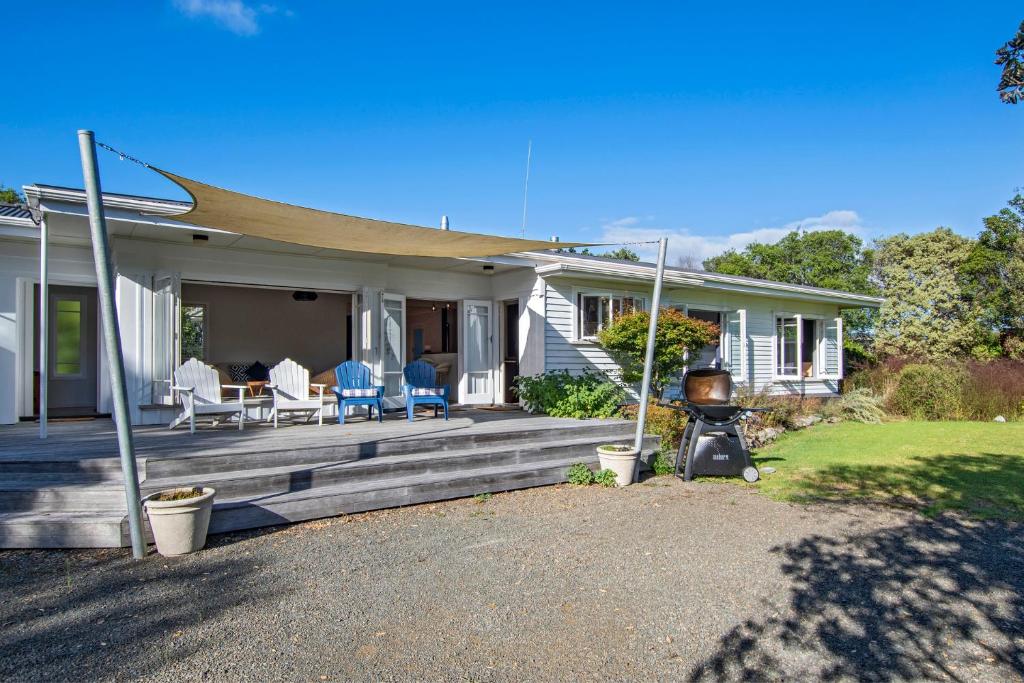 a house with a deck with chairs and a grill at Somerton - Waipu Holiday Home in Waipu Cove