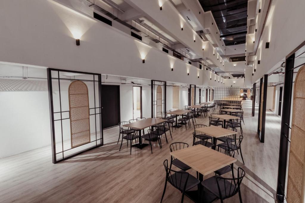 A long communal dining area with small tables, black chairs and tall windows.