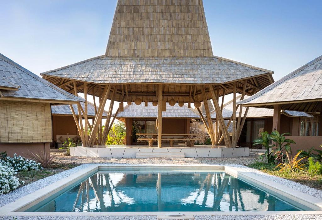 a swimming pool in front of a house with a roof at Maringi Sumba by Sumba Hospitality Foundation in Waikelo