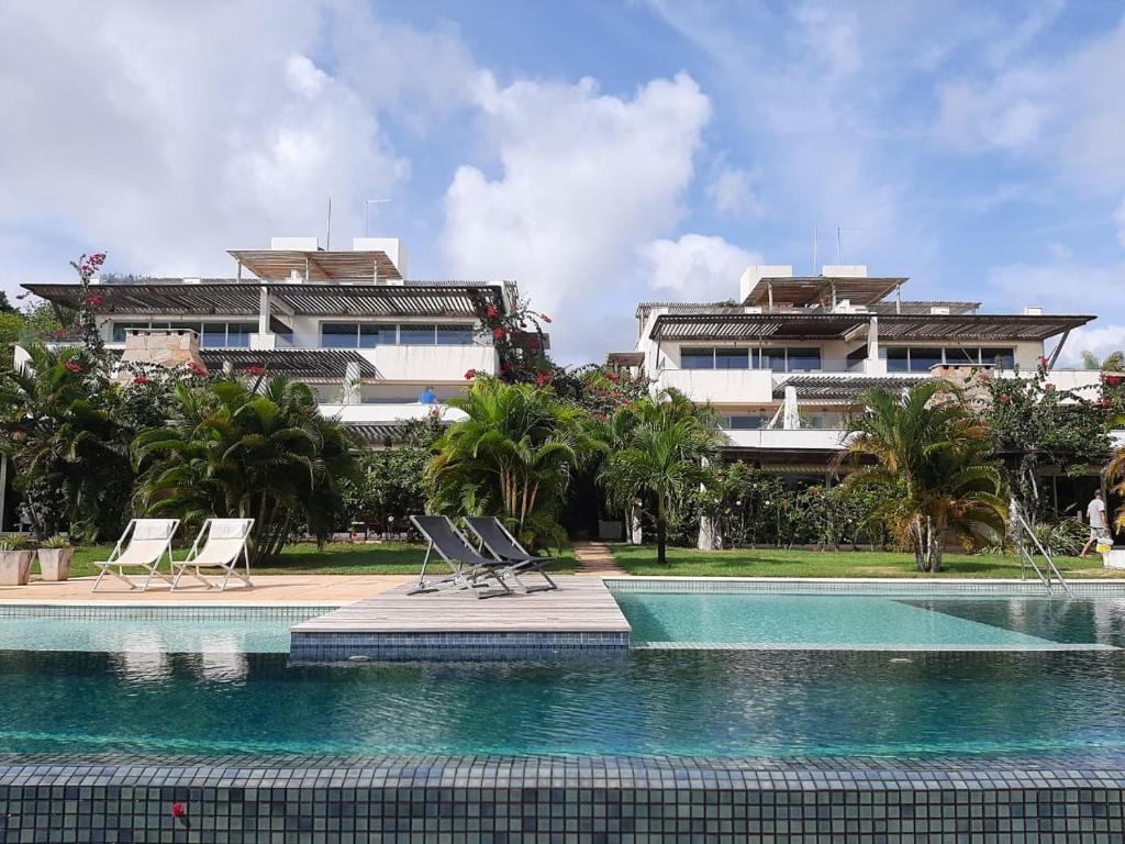 a swimming pool with two chairs and a building at Apartamentos no Pipa Residence in Pipa