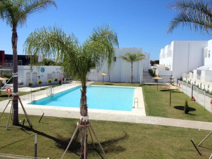 une piscine avec un palmier à côté d'un bâtiment dans l'établissement La Fontanilla Place, à Conil de la Frontera