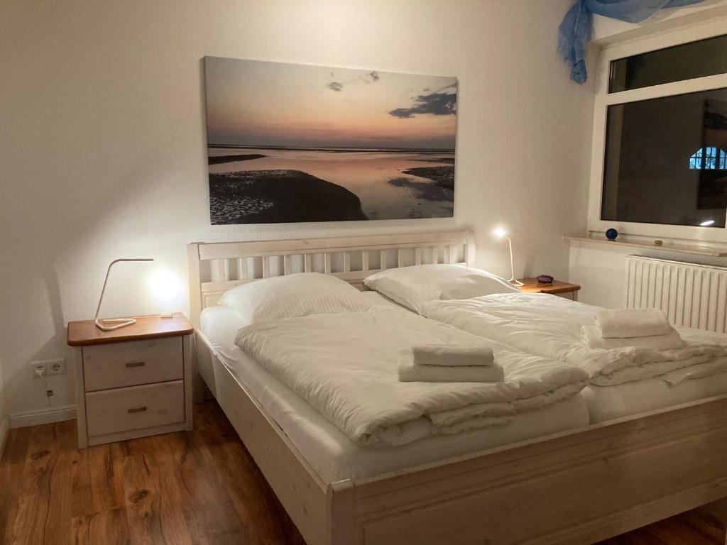 um quarto com uma cama branca e uma pintura na parede em Hellinghaus FeWo 3 Strandläufer em Wyk auf Föhr