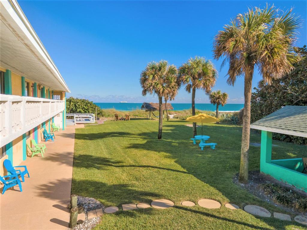 einen Garten mit Stühlen, Palmen und dem Meer in der Unterkunft South Beach Inn - Cocoa Beach in Cocoa Beach