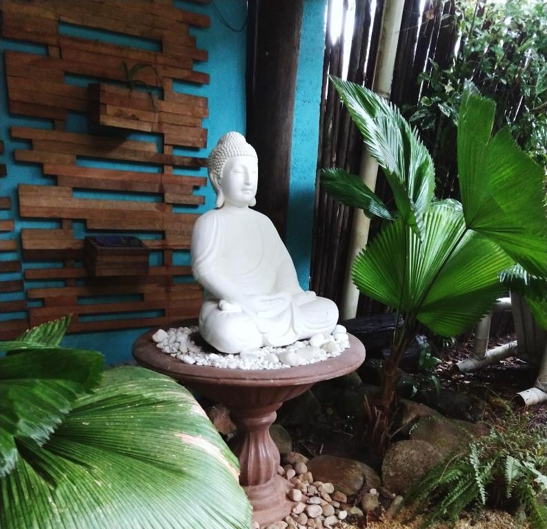 a white buddha statue sitting on a stand in a garden at Pousada Gaucha Caiobá in Matinhos