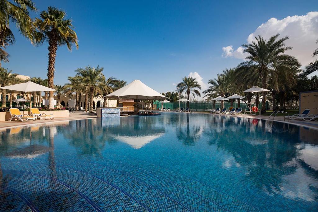 a large swimming pool with palm trees and umbrellas at Metropolitan Al Mafraq Hotel in Abu Dhabi