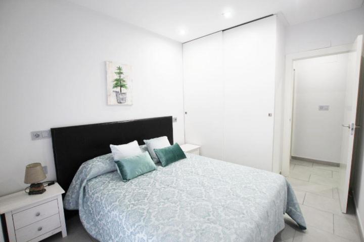 a white bedroom with a large bed with blue pillows at Apartamento Bajo 2 Dúplex Marjal playa centro de Guardamar in Guardamar del Segura