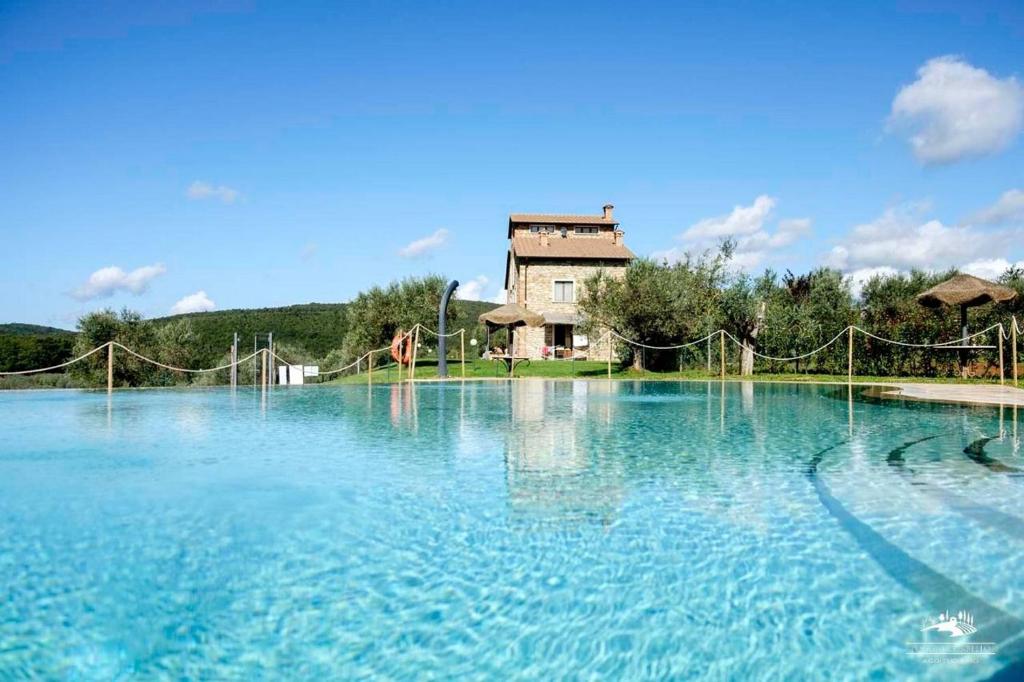 una grande piscina di acqua blu con un edificio sullo sfondo di Tenuta La Tabaccaia a La Pesta
