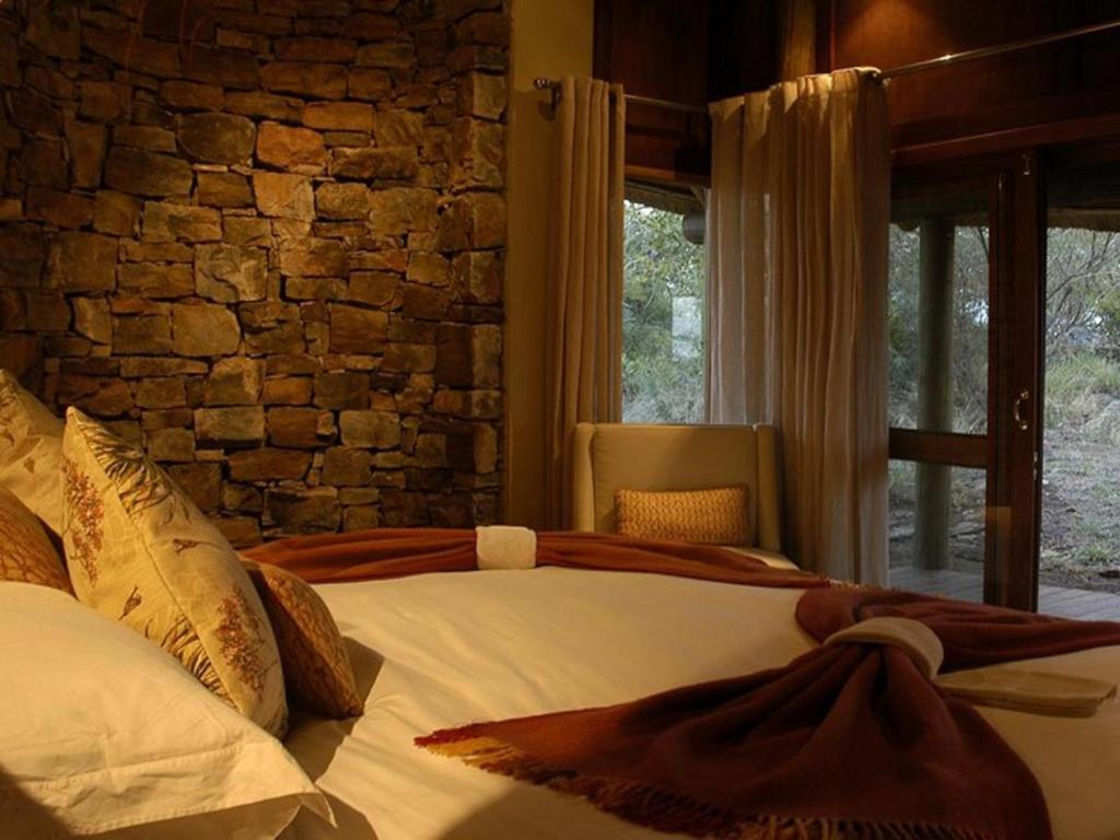 - une chambre avec un lit et un mur en pierre dans l'établissement Buffalo Ridge Safari Lodge, à Madikwe Game Reserve