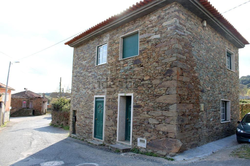 a stone building with green doors on a street at Casinha de Nogueirinha in Macedo de Cavaleiros