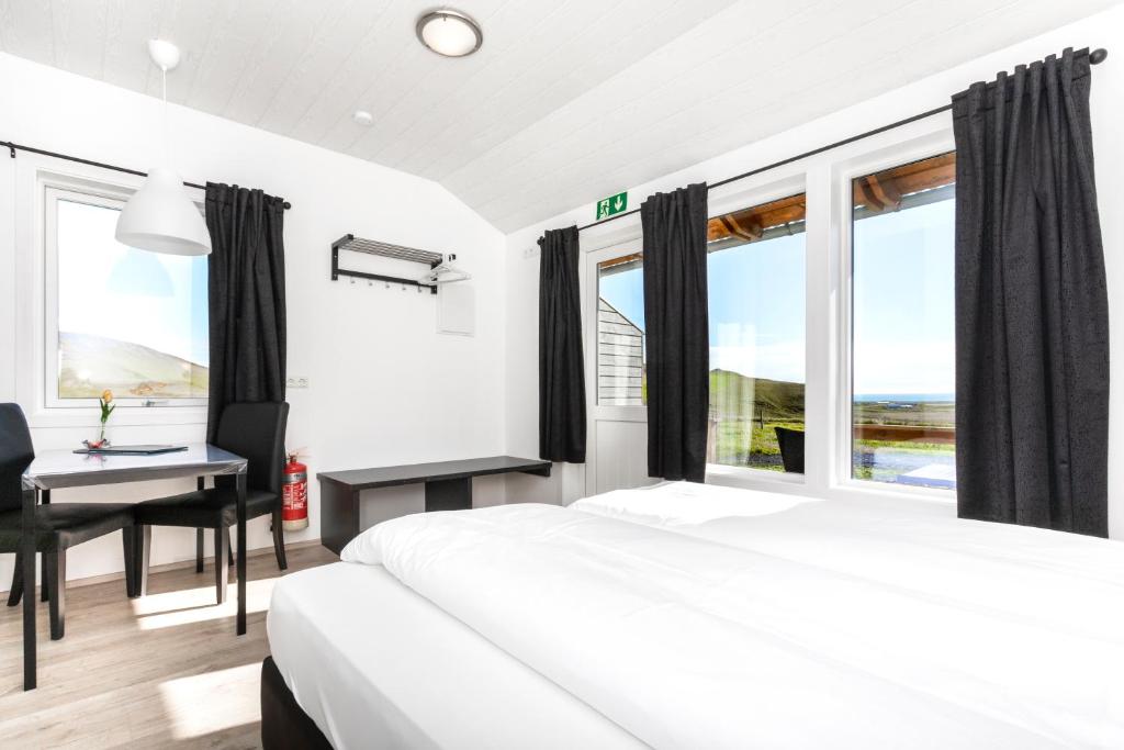 um quarto com uma cama, uma secretária e janelas em Hvammból Guesthouse em Vík
